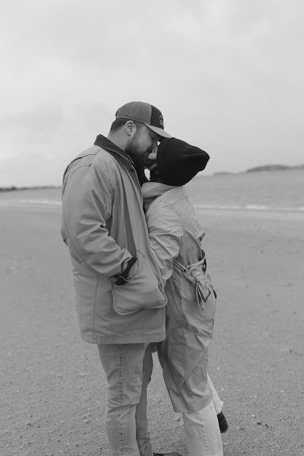 Intimate black and white engagement portrait of a couple standing close together by the ocean.
