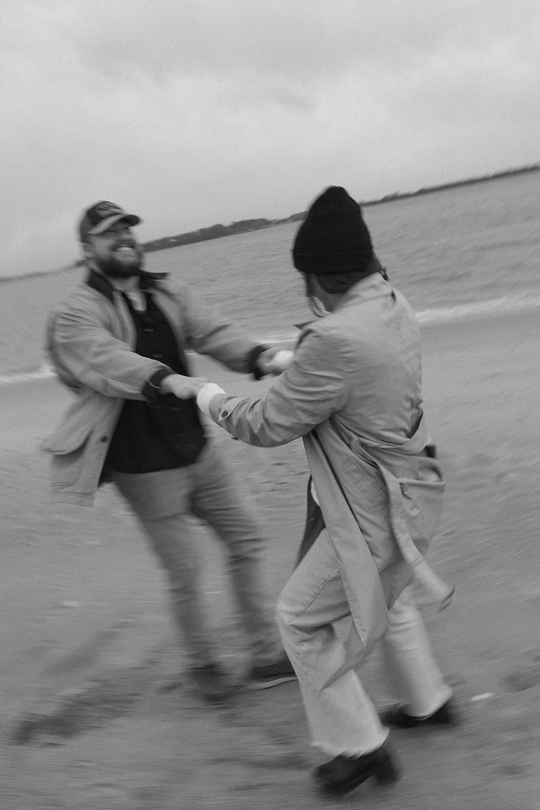 Candid engagement photo of a couple laughing and twirling on the beach during a winter engagement session.
