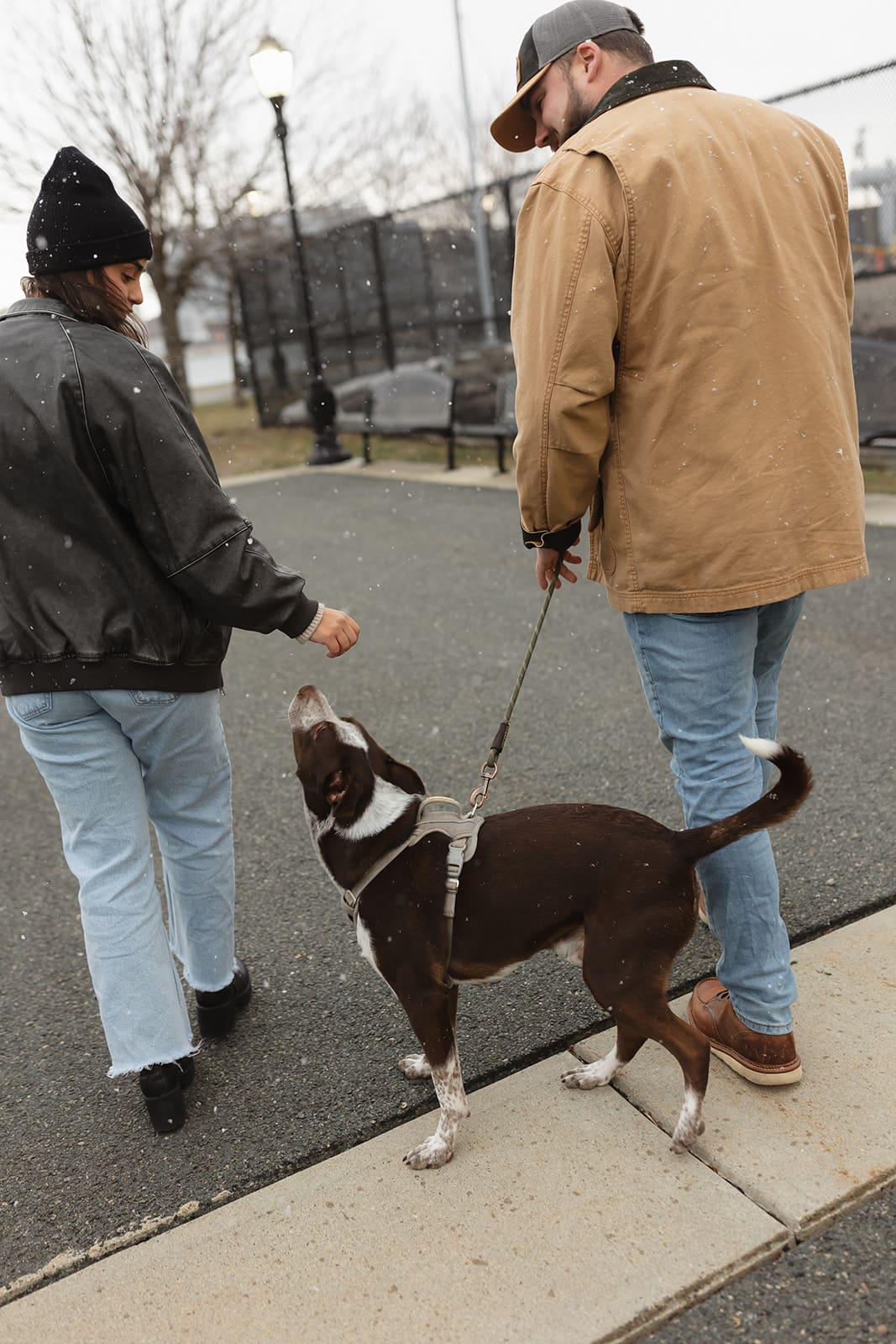 Couple walking their dog together along a waterfront path during a candid engagement session.
