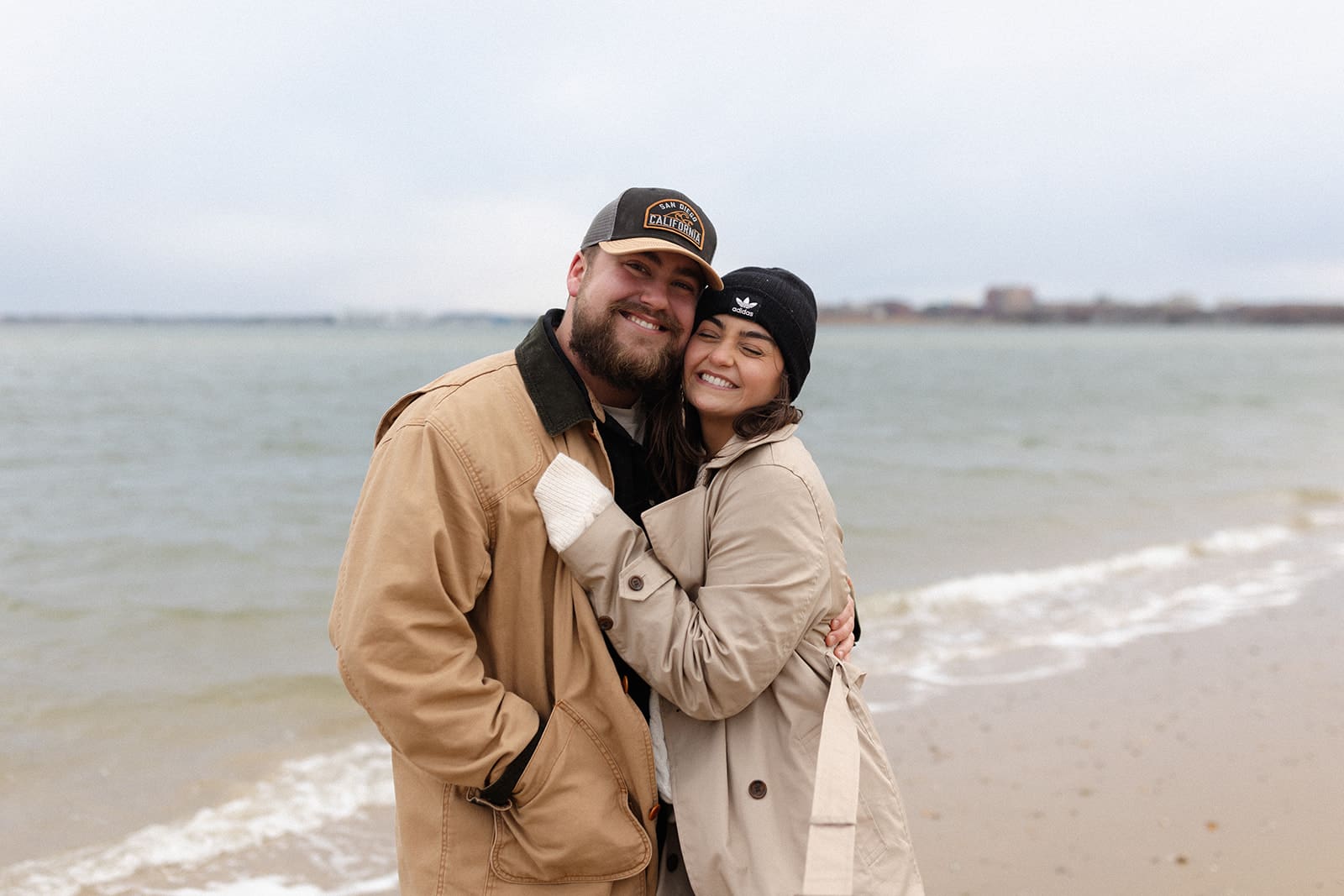 Romantic engagement portrait of a couple standing beside colorful kayaks near a coastal cottage at golden hour.
