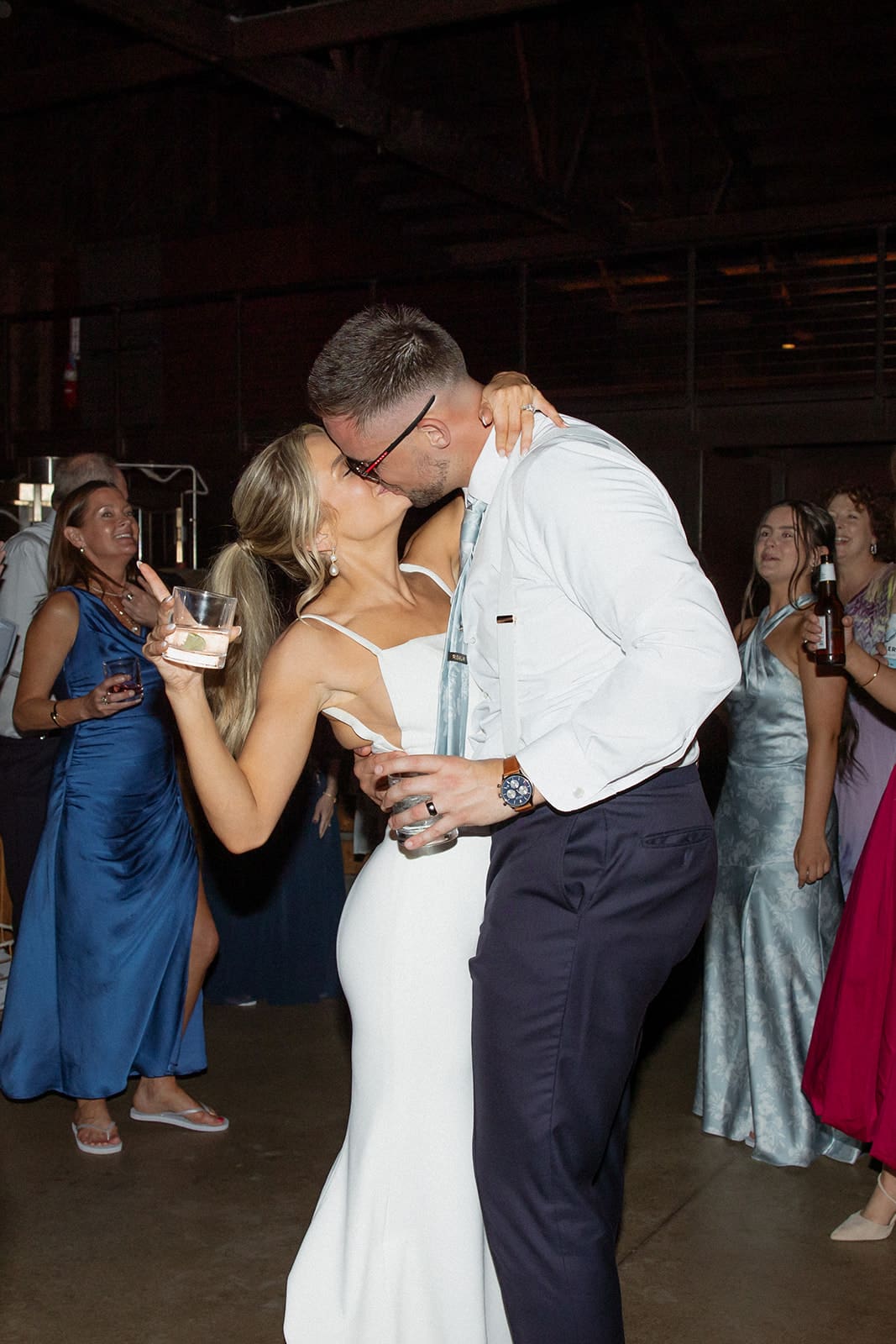 Bride and groom dancing and celebrating with drinks on the dance floor surrounded by wedding guests.