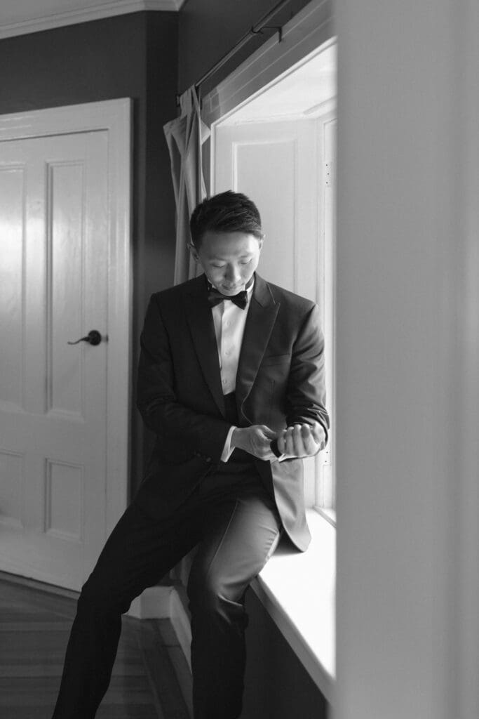 Groom adjusting his cufflinks by a window in a quiet getting ready moment
