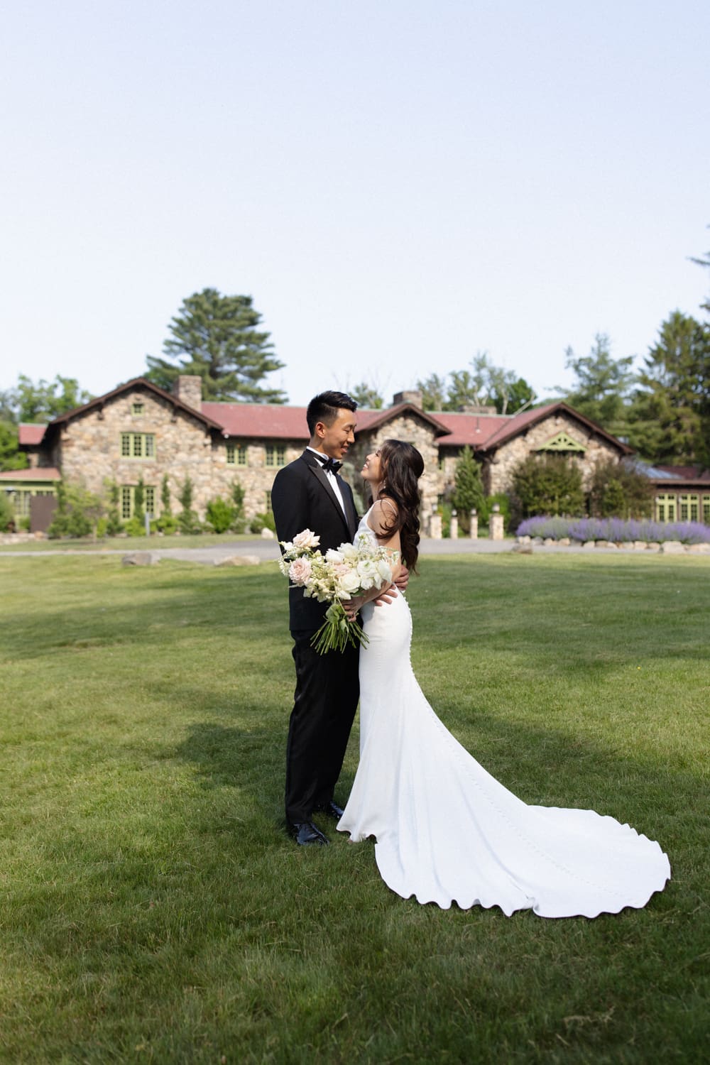 Bride and groom embrace on an open lawn with a stone estate in the background at a Massachusetts wedding venue
