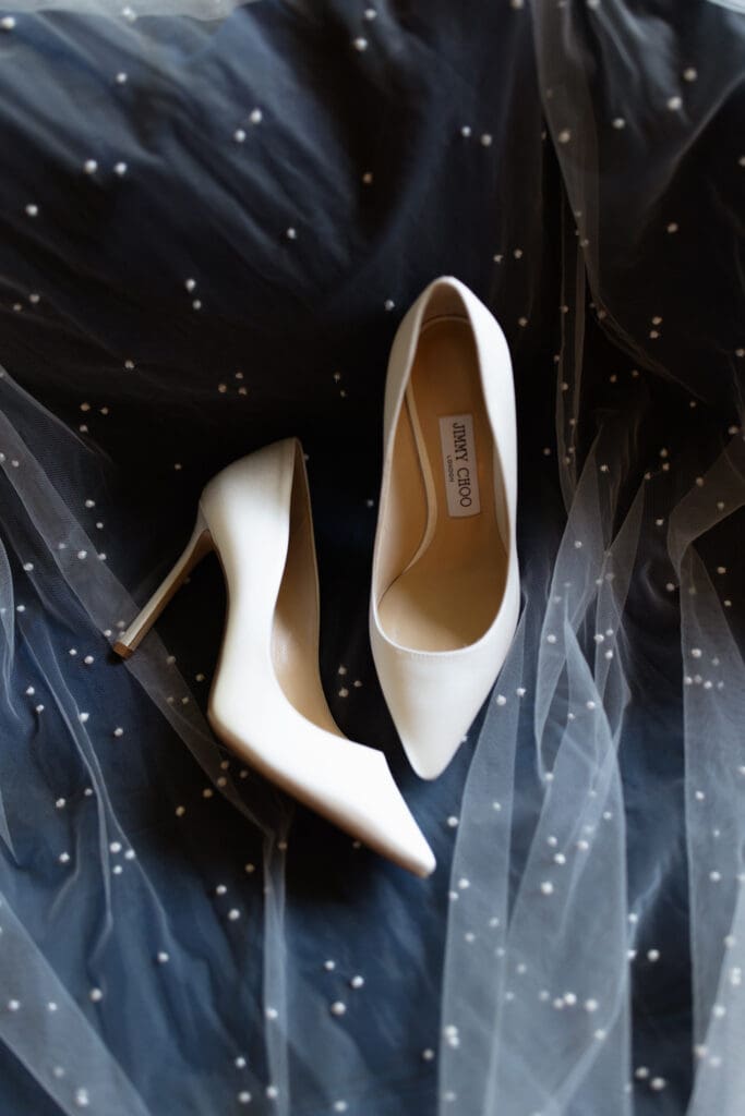 White bridal heels resting on a soft veil with delicate detailing
