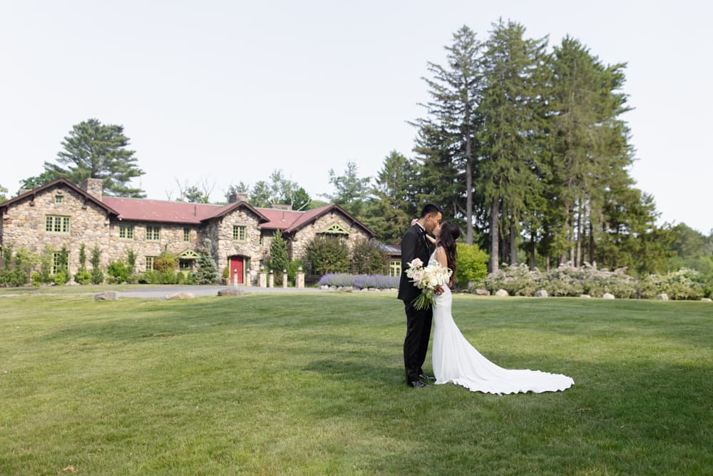 Bride and groom sharing a kiss on an open lawn with a stone estate in the background at a Massachusetts wedding venue