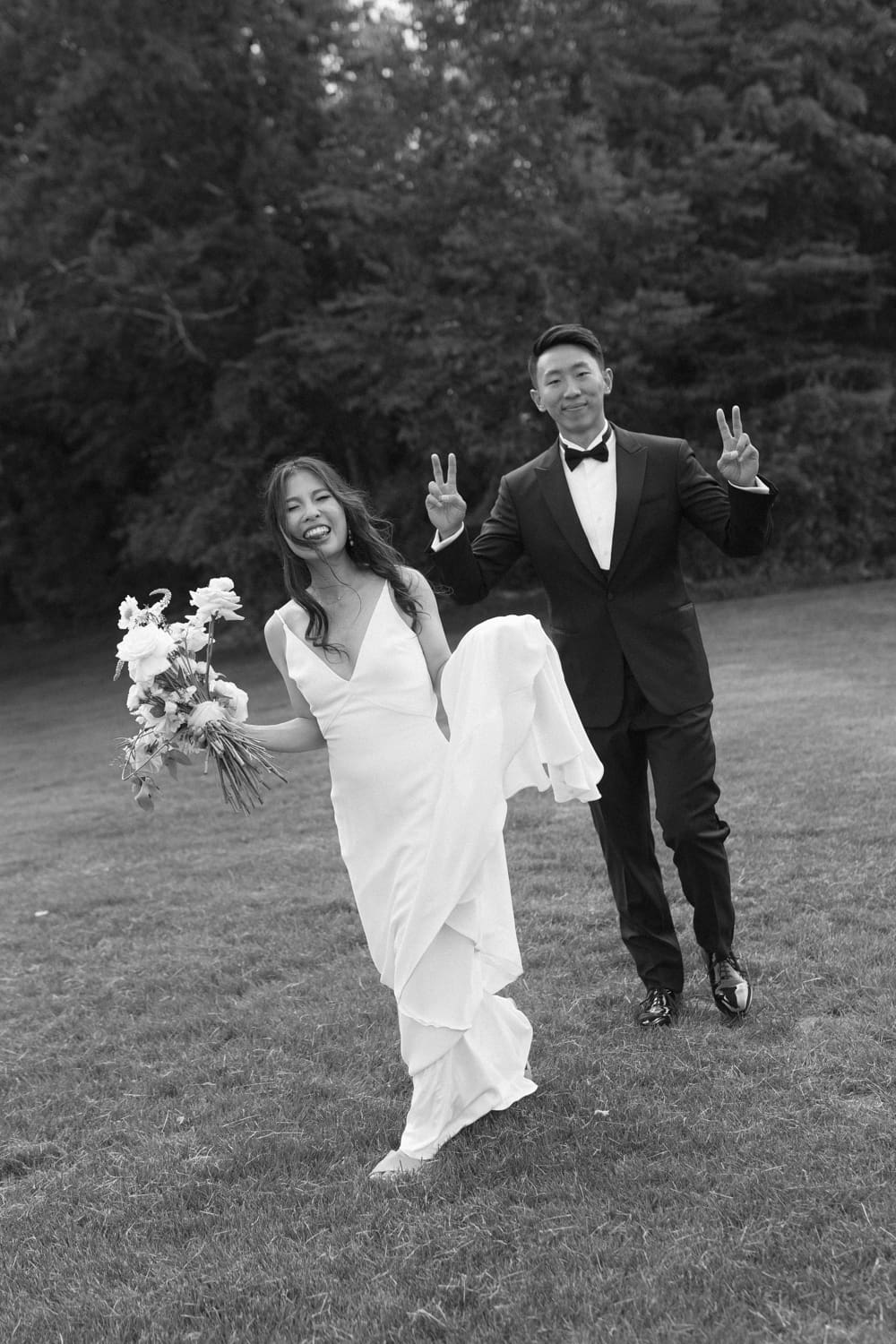 Playful moment of bride and groom walking through a field, laughing as they celebrate just married
