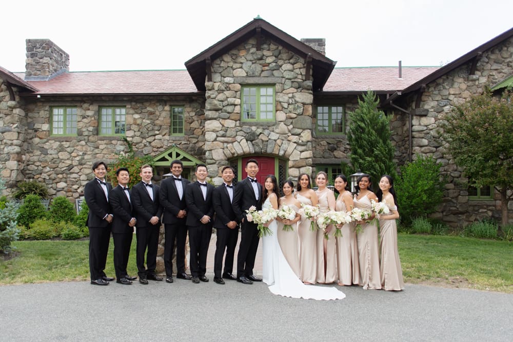 Wedding party standing together in front of a stone estate at a Massachusetts wedding venue, holding neutral-toned bouquets
