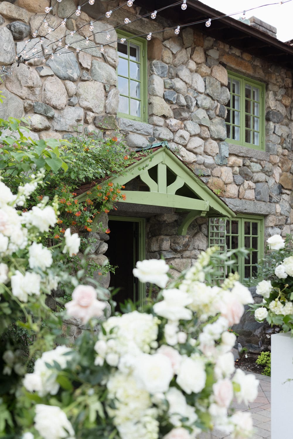 Stone estate exterior with green trim and soft floral arrangements framing the entrance at a Massachusetts wedding venue