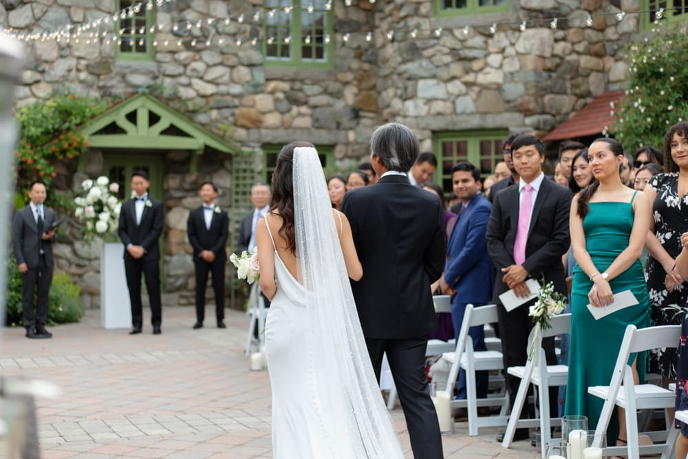 Bride walking down the aisle with her father during an outdoor courtyard ceremony at a Massachusetts wedding venue