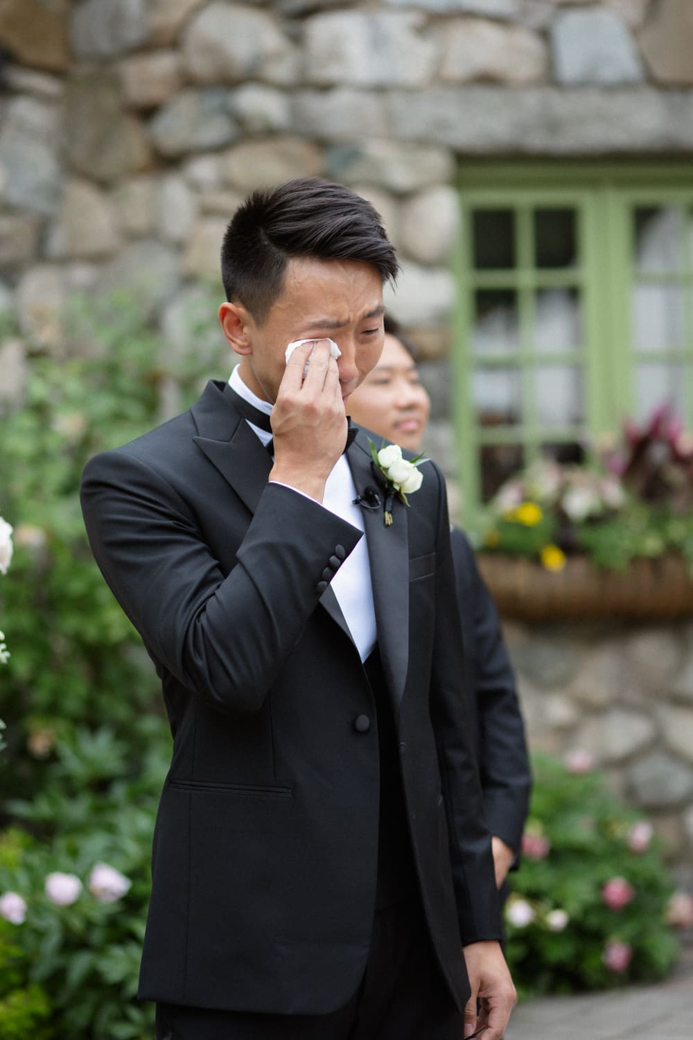 Groom wiping away tears during an emotional outdoor wedding ceremony in a garden courtyard