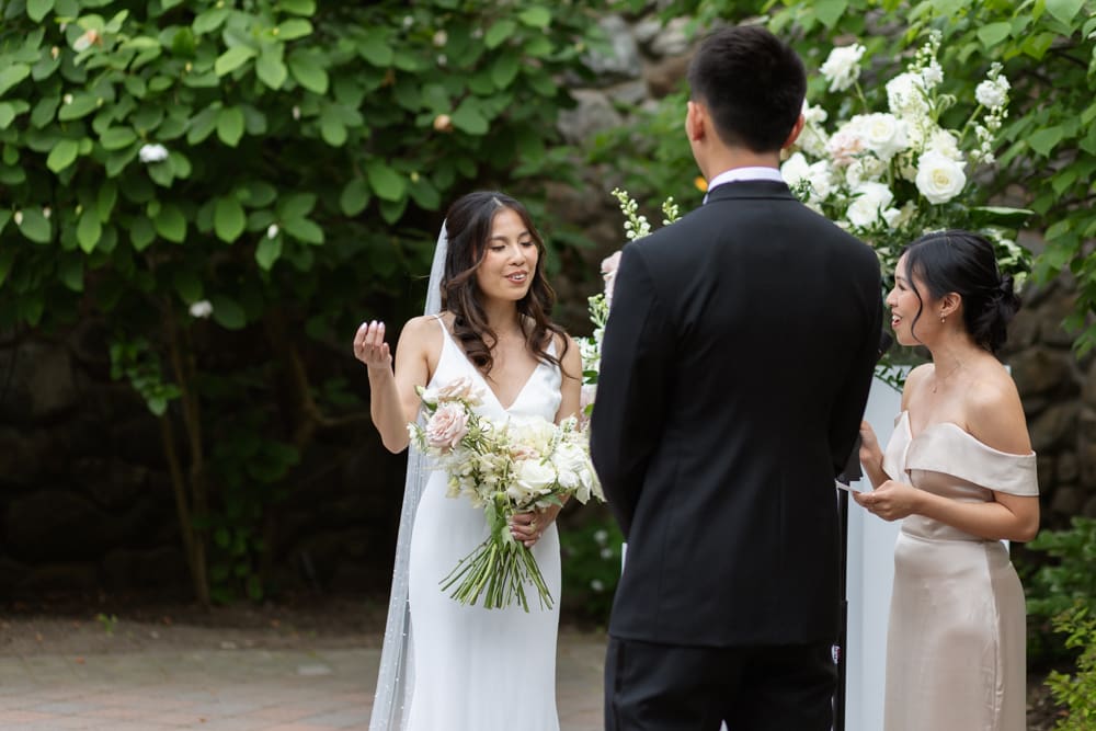 Bride speaking during the ceremony while holding her bouquet, with her partner and officiant standing nearby
