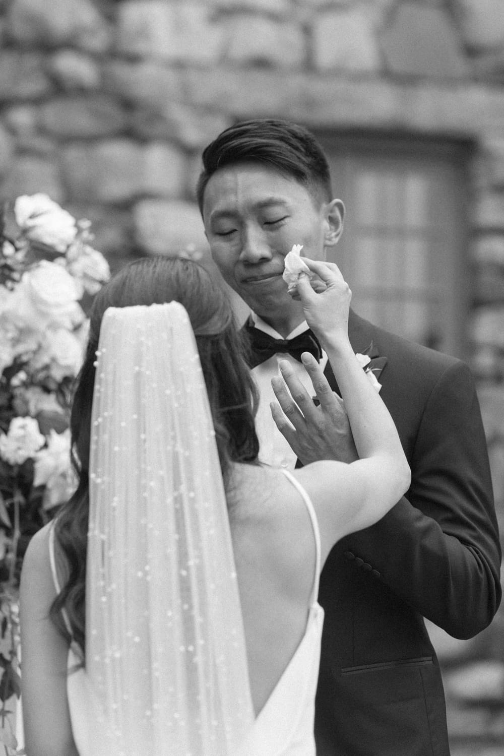Bride gently wiping tears from the groom’s face during an emotional vow exchange in a garden courtyard
