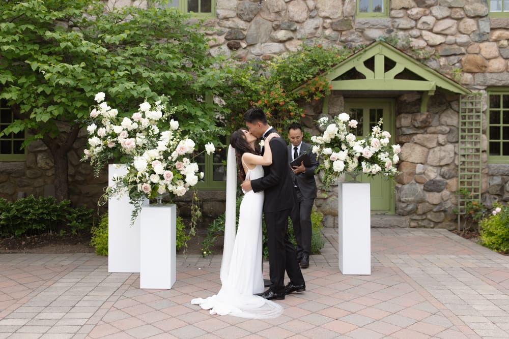 Bride and groom sharing a kiss during their ceremony in front of a stone building at a Massachusetts wedding venue
