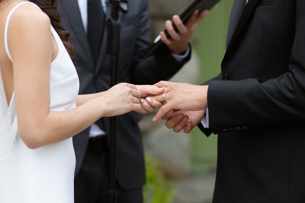 Bride placing a ring on the groom’s finger during an outdoor ceremony at a Massachusetts wedding venue
