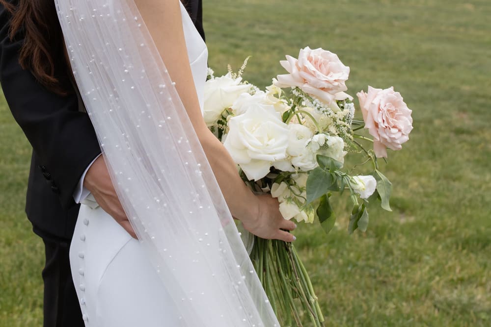 Close-up of bride’s veil and bouquet with soft white and blush flowers against a natural green backdrop
