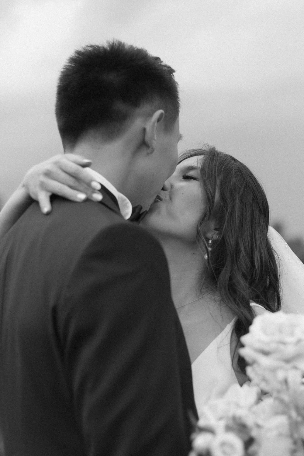 Black and white close-up of bride and groom sharing a kiss, holding each other closely
