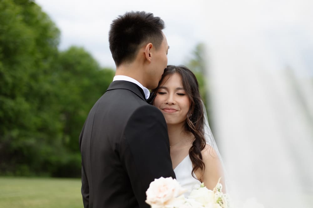 Groom kissing the bride’s forehead as she smiles with her eyes closed, holding her bouquet
