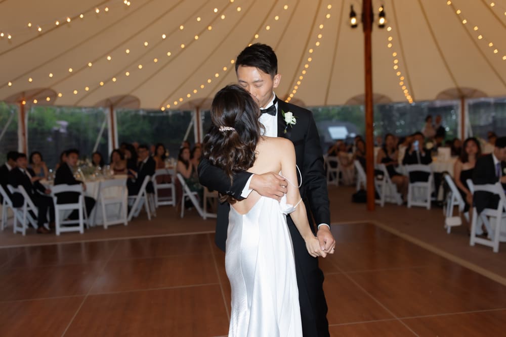 Bride and groom sharing their first dance under string lights inside a tented reception
