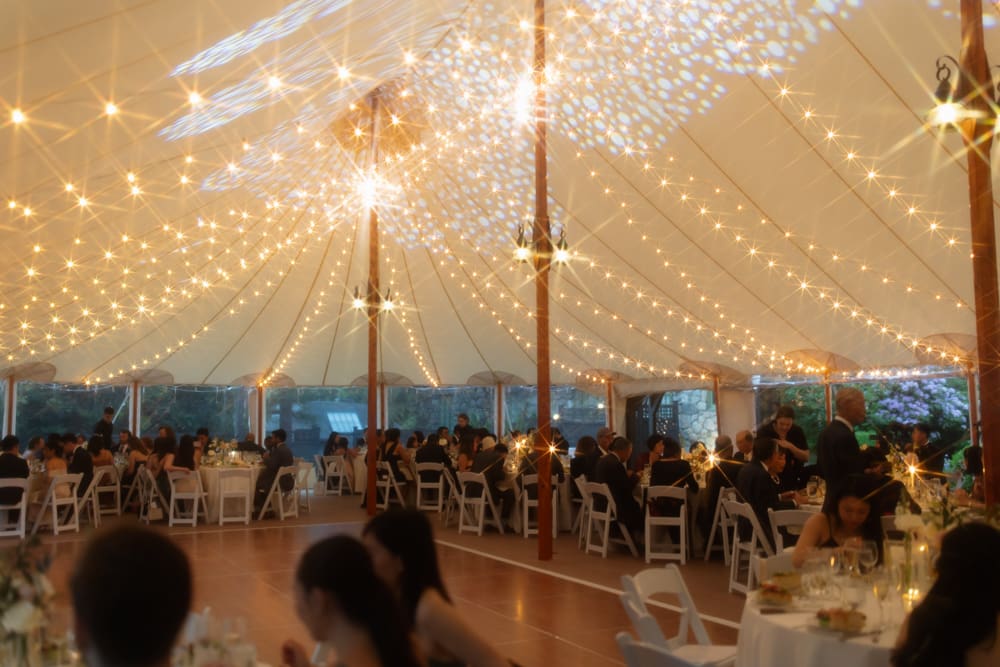 Reception tent filled with guests seated under warm string lights during dinner at a Massachusetts wedding venue