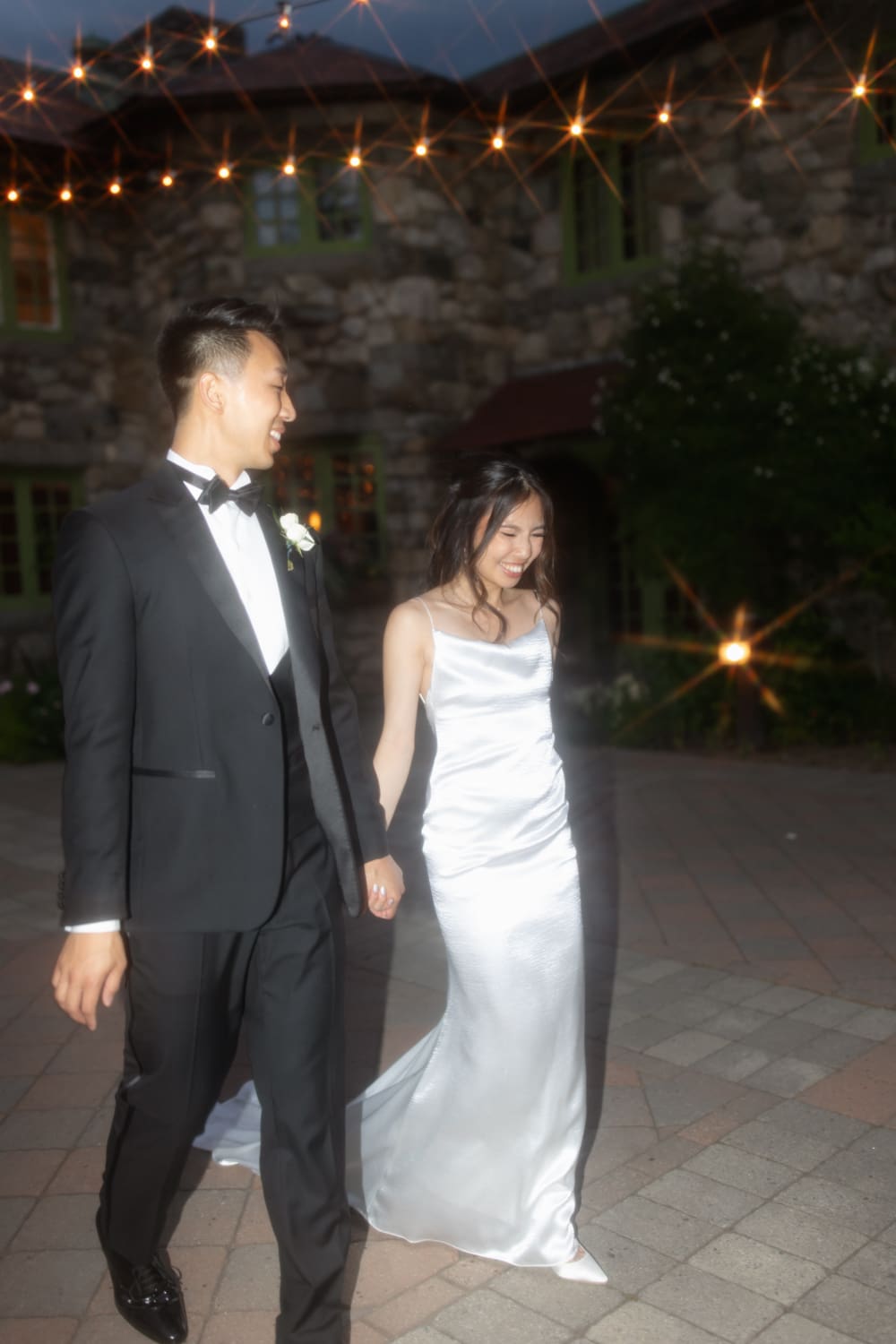 Bride and groom walking hand in hand under glowing string lights during their evening reception at a Massachusetts wedding venue
