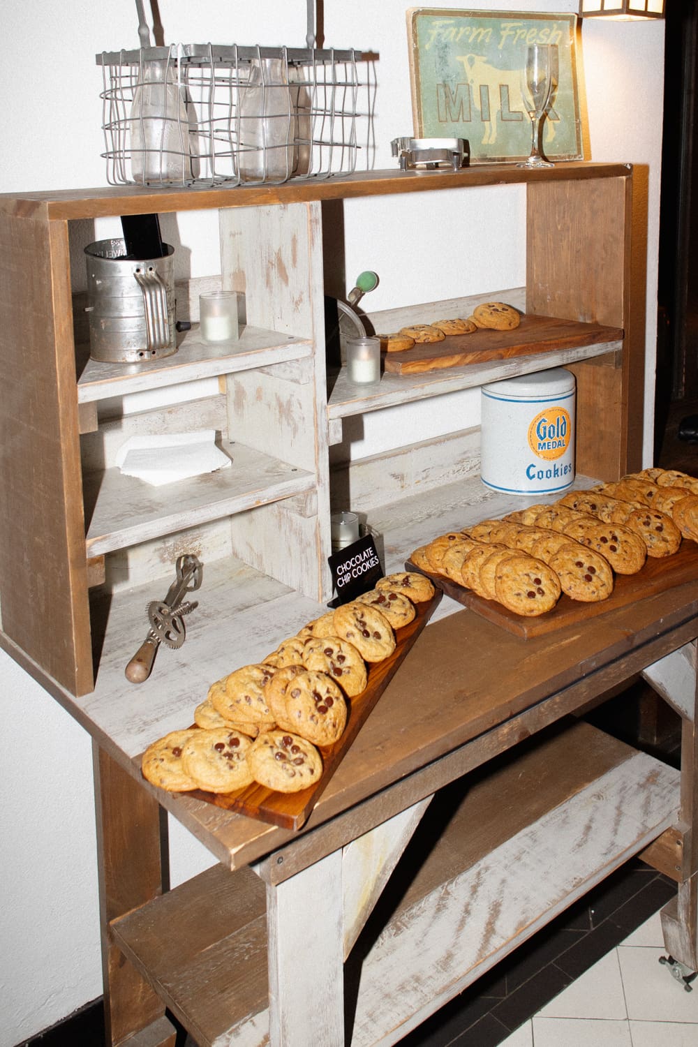 Late-night cookie display with trays of chocolate chip cookies and milk bottles on a rustic wooden shelf