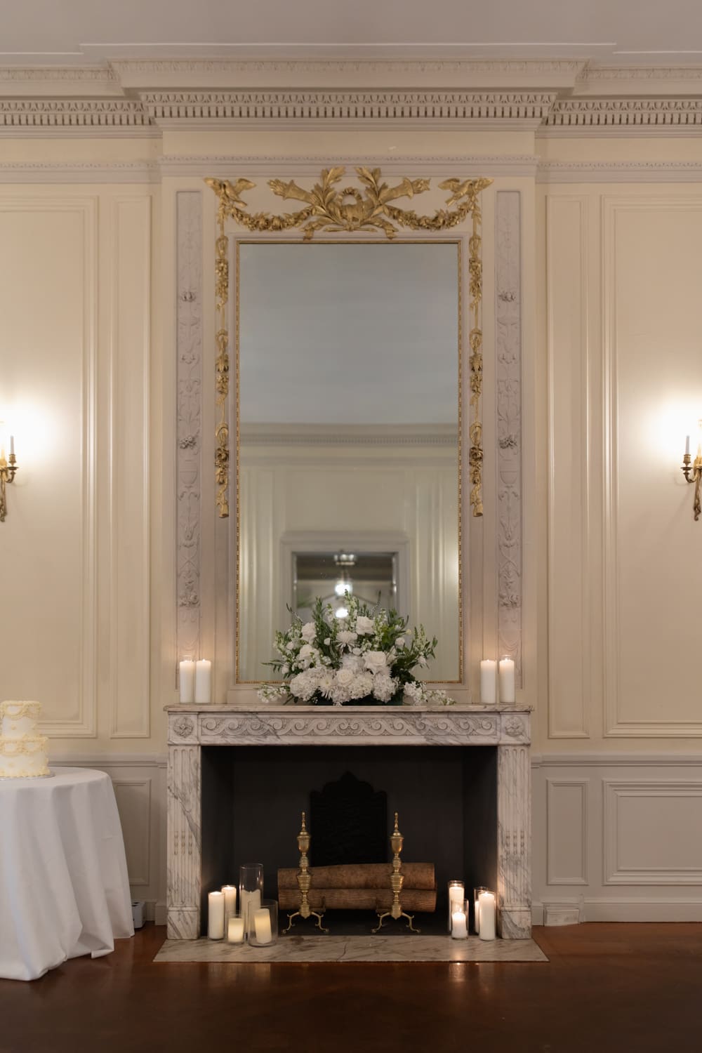Elegant fireplace mantel with white florals, candles, and a gilded mirror inside a refined wedding venue in Rhode Island.
