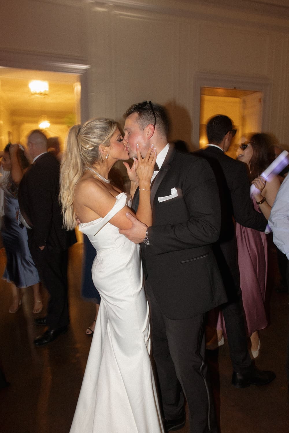 Bride and groom sharing a kiss on the dance floor surrounded by guests during the reception.