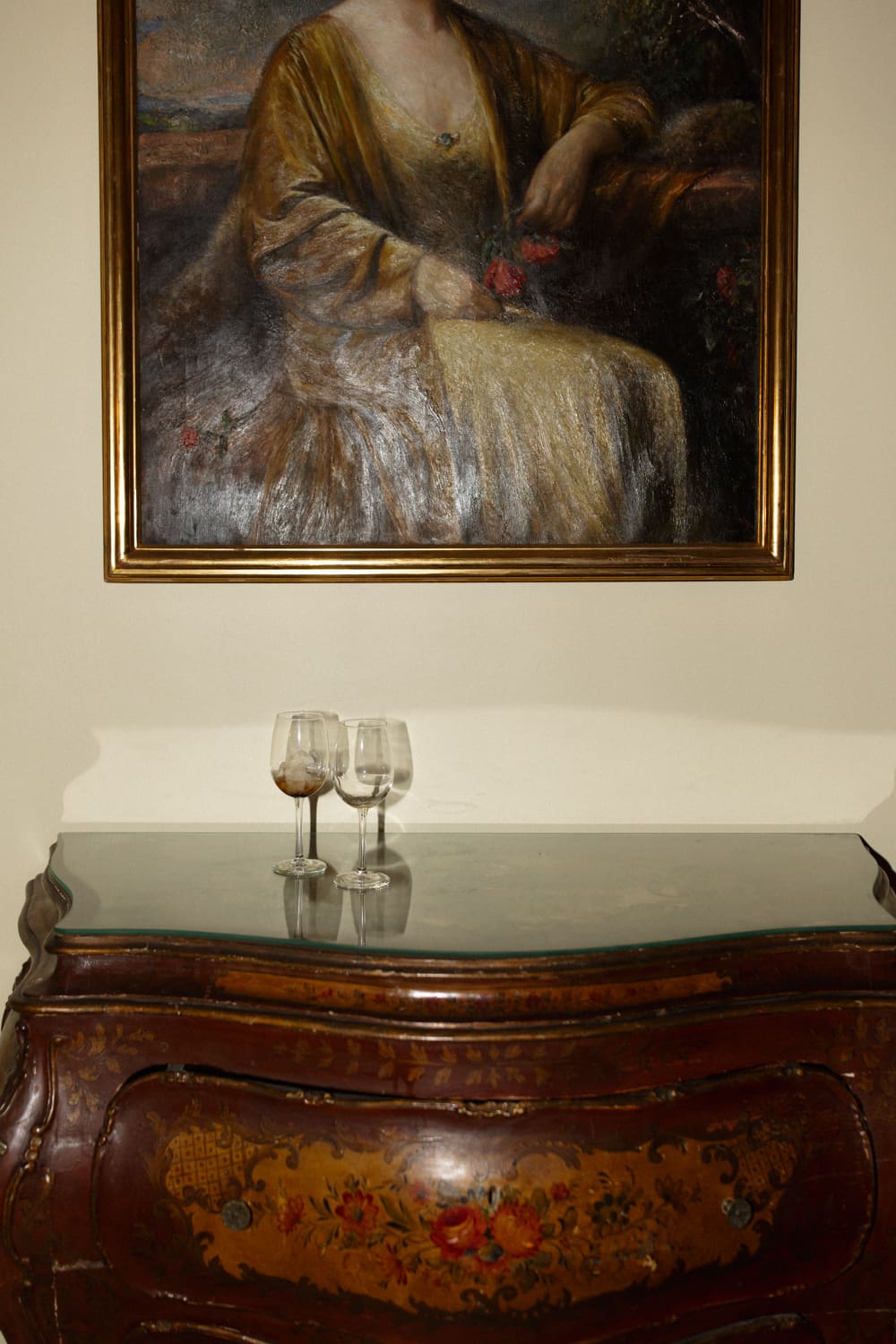 Antique wooden console with painted details and glassware beneath a framed portrait inside a wedding venue in Rhode Island.
