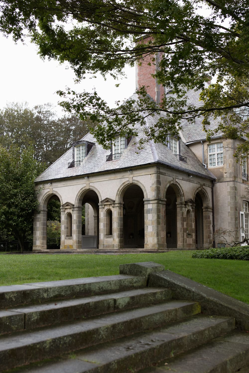 Wide view of a stone carriage house with arched openings and surrounding greenery at a wedding venue in Rhode Island.
