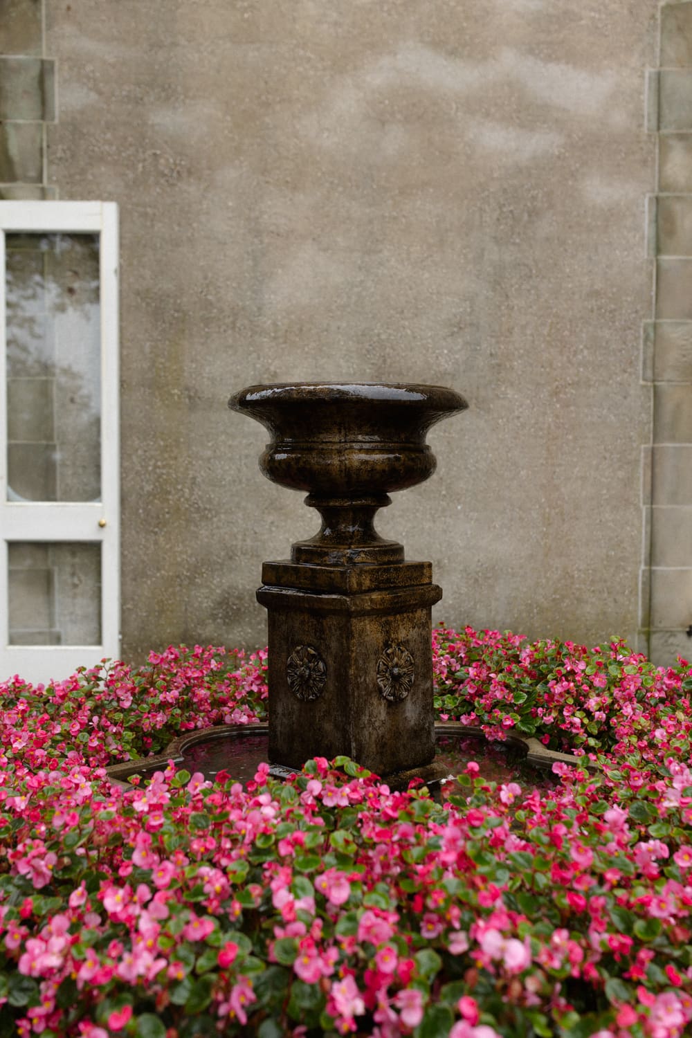 Stone fountain surrounded by pink flowers in a garden setting at a wedding venue in Rhode Island.
