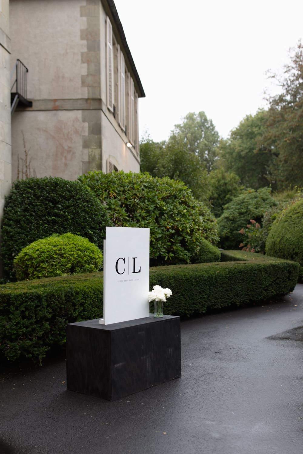 Minimal welcome sign with initials displayed along a garden path, marking the entrance to a wedding venue in Rhode Island.
