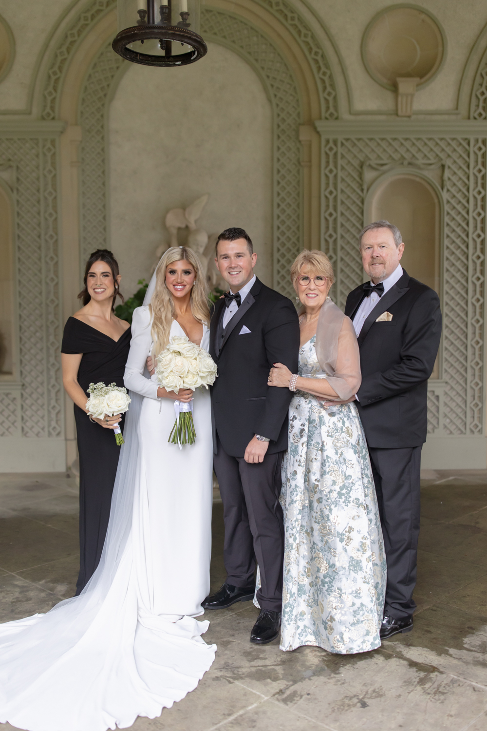 Bride and groom posing with family beneath an arched stone alcove at a wedding venue in Rhode Island.