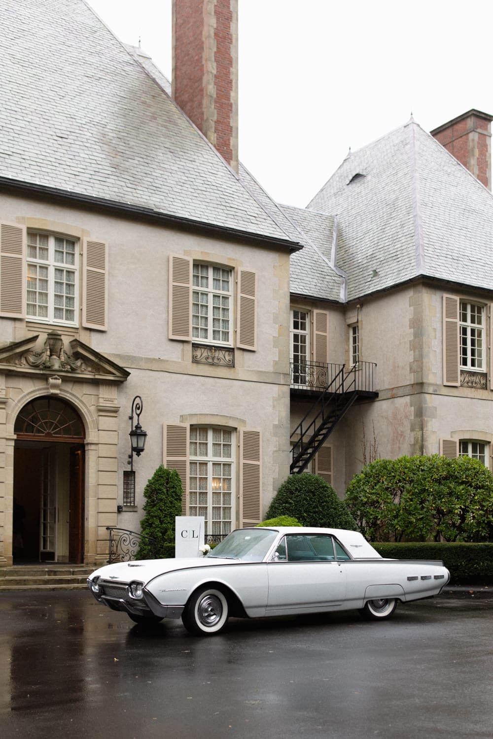 Classic getaway car parked outside a European-style mansion with soft gray shutters at a wedding venue in Rhode Island.

