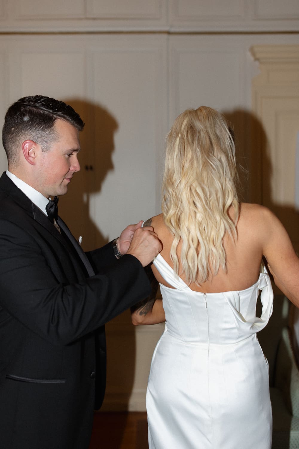 Groom helping adjust the back of the bride’s dress during the reception.