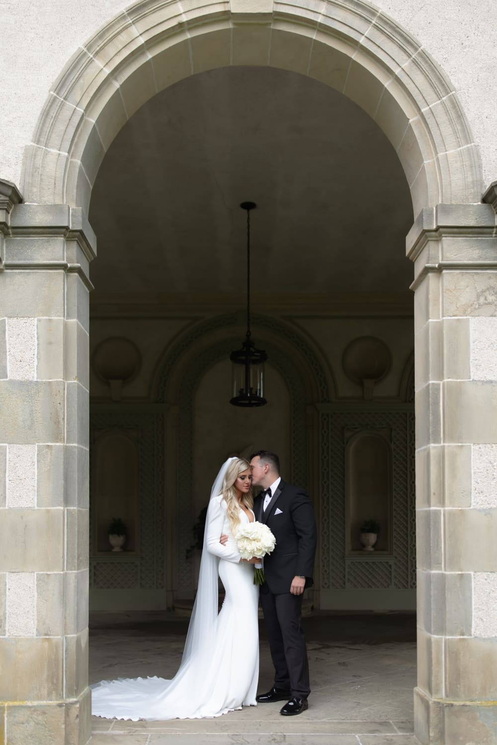 Bride and groom standing close beneath a stone archway, sharing a quiet moment outside a wedding venue in Rhode Island.
