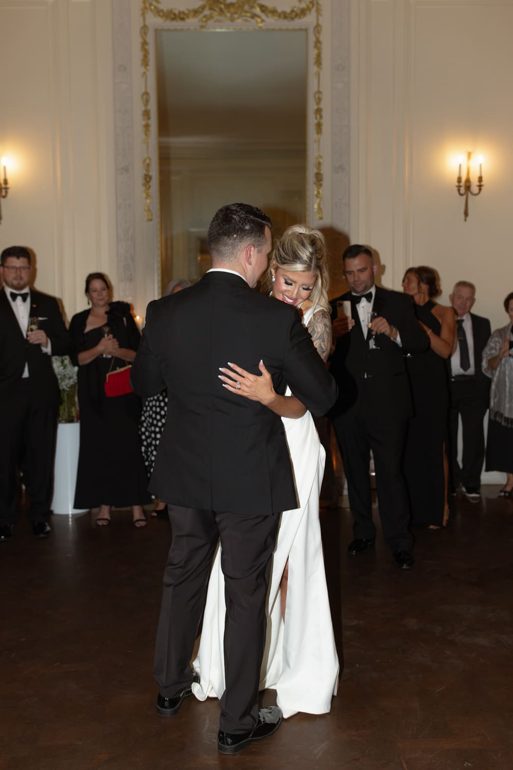 Bride and groom sharing their first dance in a softly lit ballroom with guests watching.