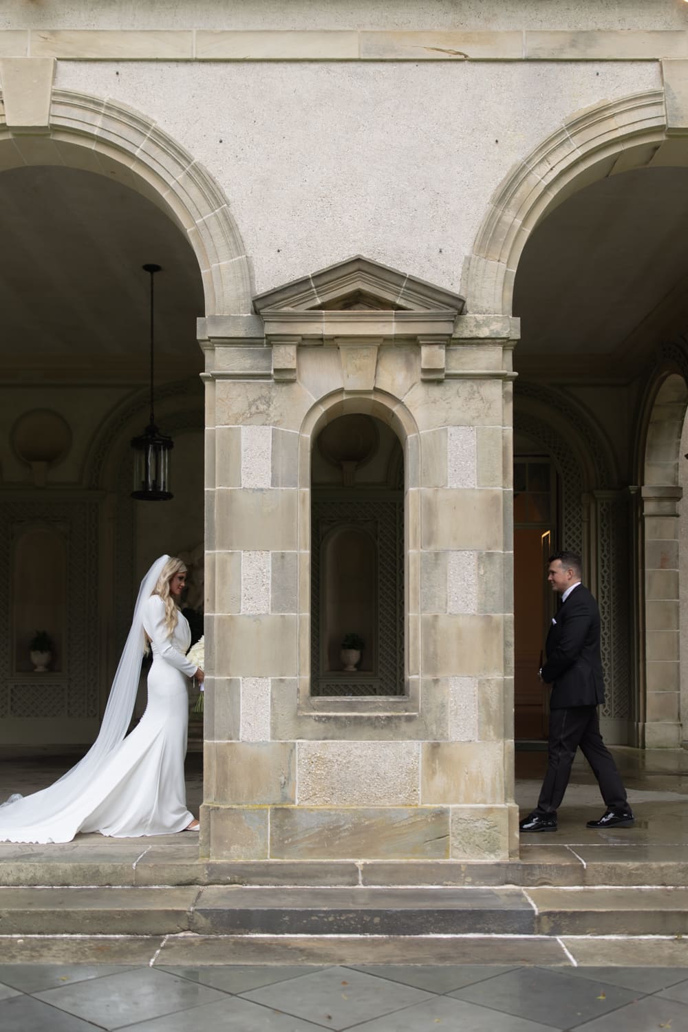 Bride and groom approaching each other from opposite sides of a stone walkway for their first look at a wedding venue in Rhode Island.
