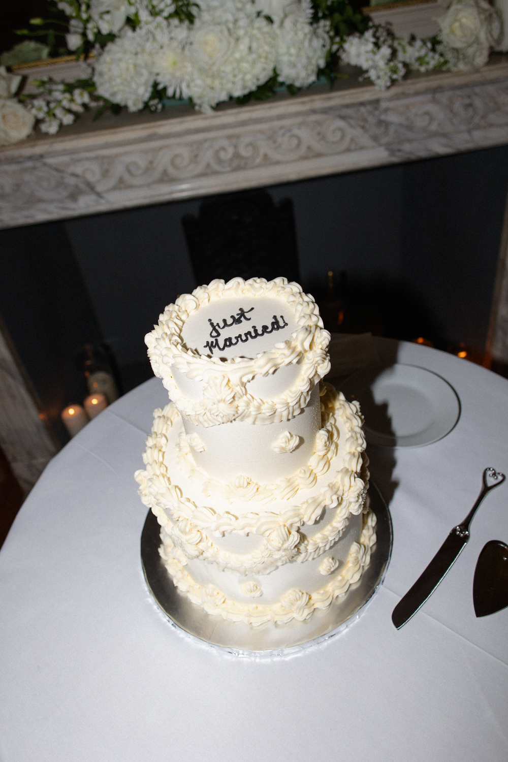Close-up of a tiered white wedding cake with piped details and “just married” written on top.
