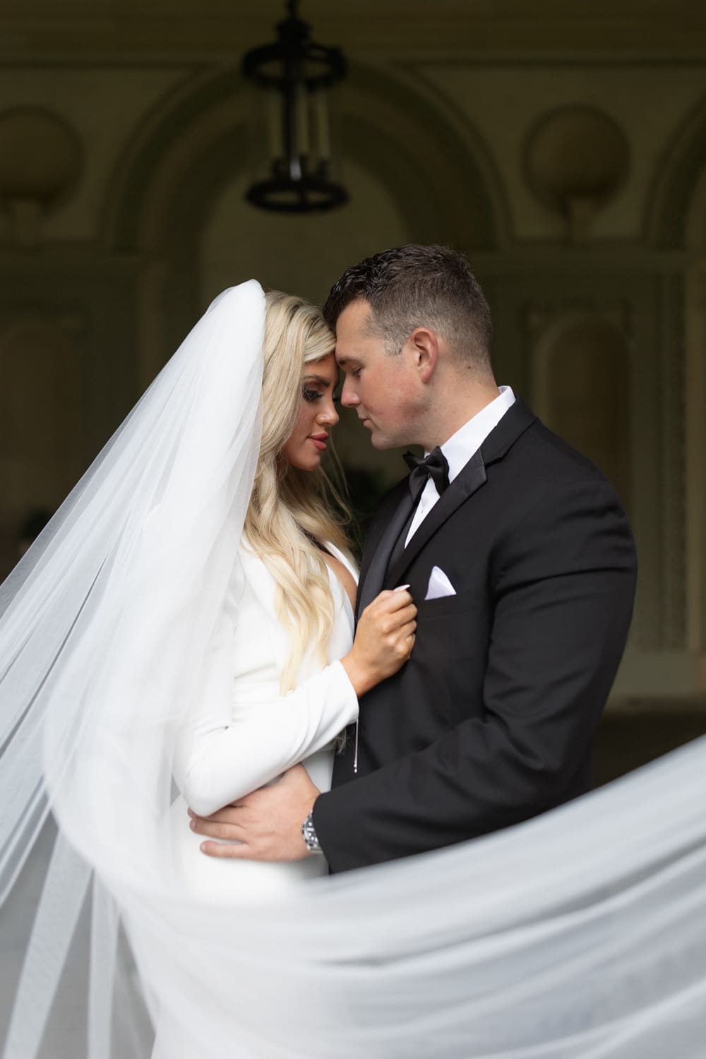 Bride and groom standing close together beneath a flowing veil in a quiet portrait at a wedding venue in Rhode Island.