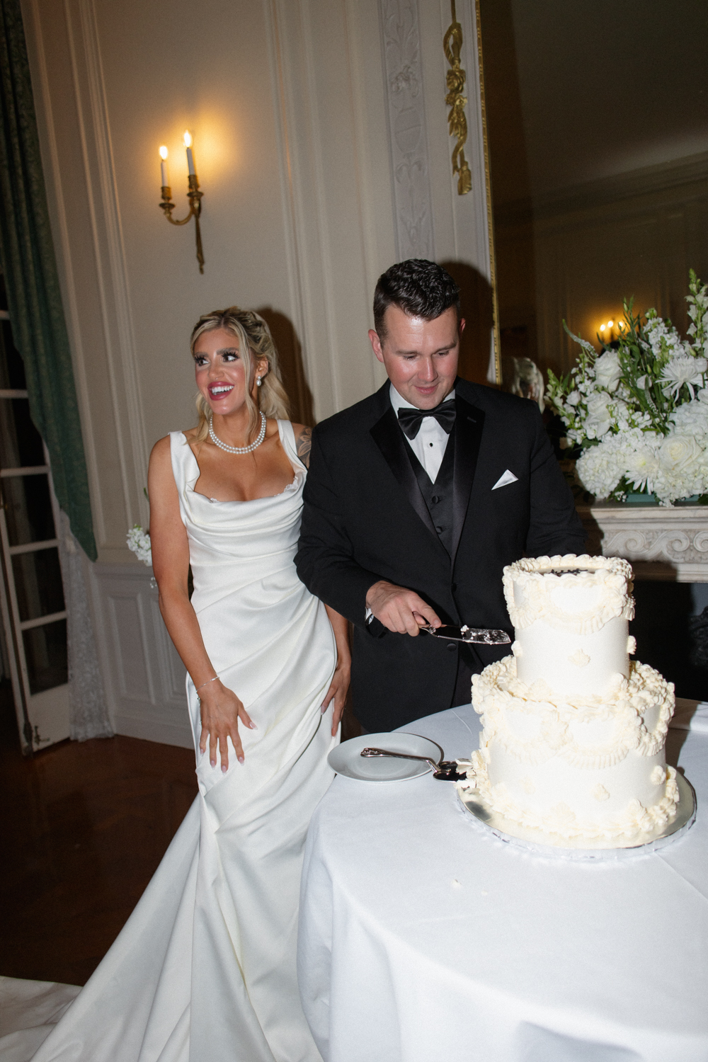 Bride smiling beside the groom as he cuts the wedding cake at a wedding venue in Rhode Island.