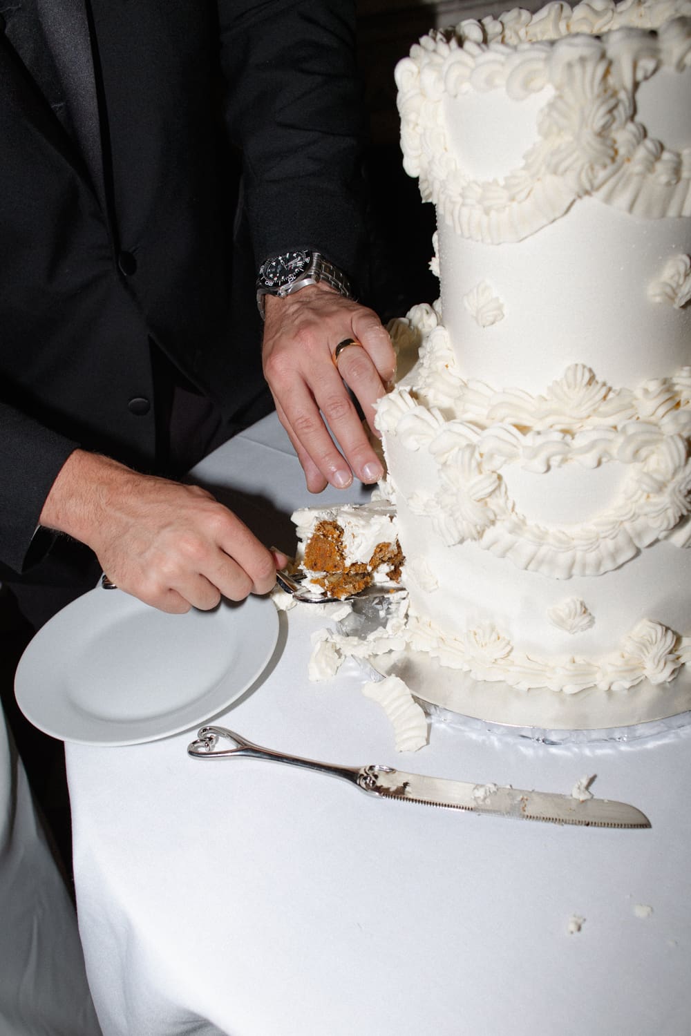 Groom cutting into a tiered white wedding cake during the reception.