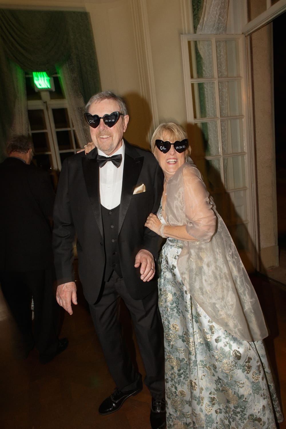 Older couple in formal attire smiling and wearing heart-shaped sunglasses on the dance floor at a wedding venue in Rhode Island.