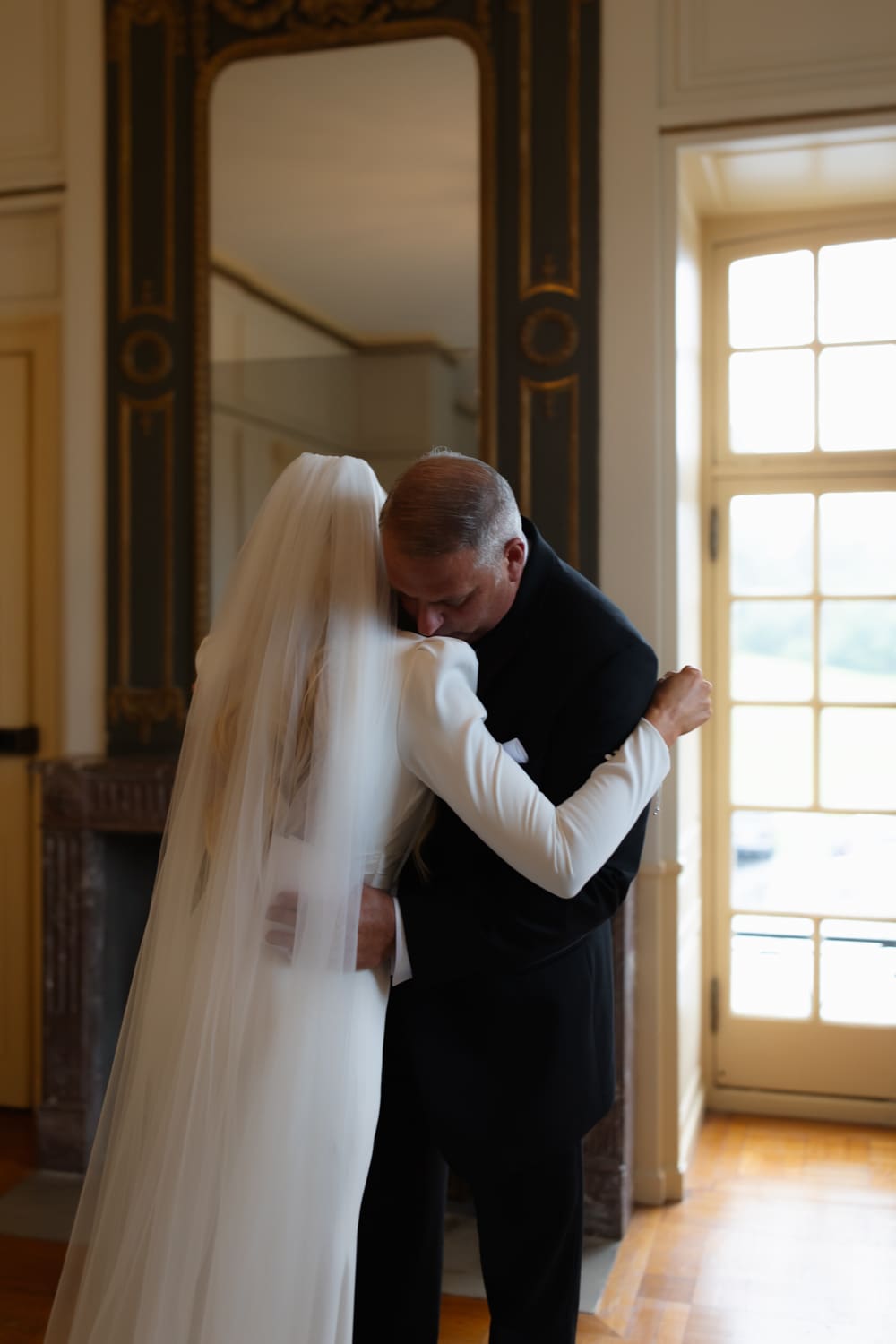 Bride embracing her father in a quiet moment before the ceremony, standing near a window inside a wedding venue in Rhode Island.
