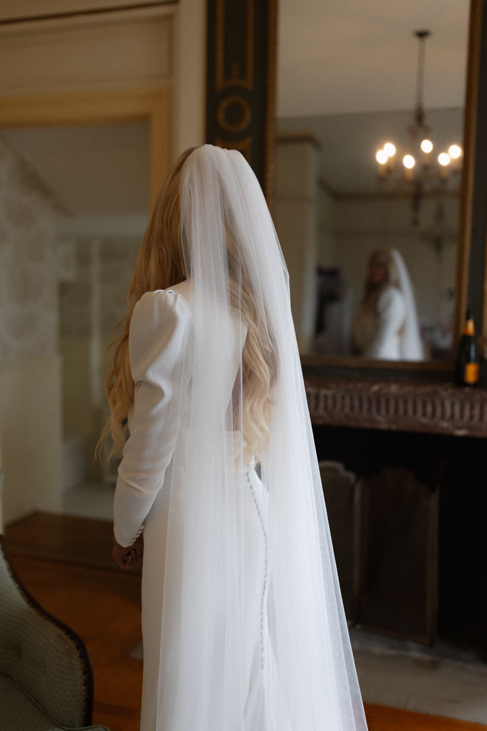 Bride standing in a softly lit room with her veil falling down her back, reflected in a mirror inside a wedding venue in Rhode Island.
